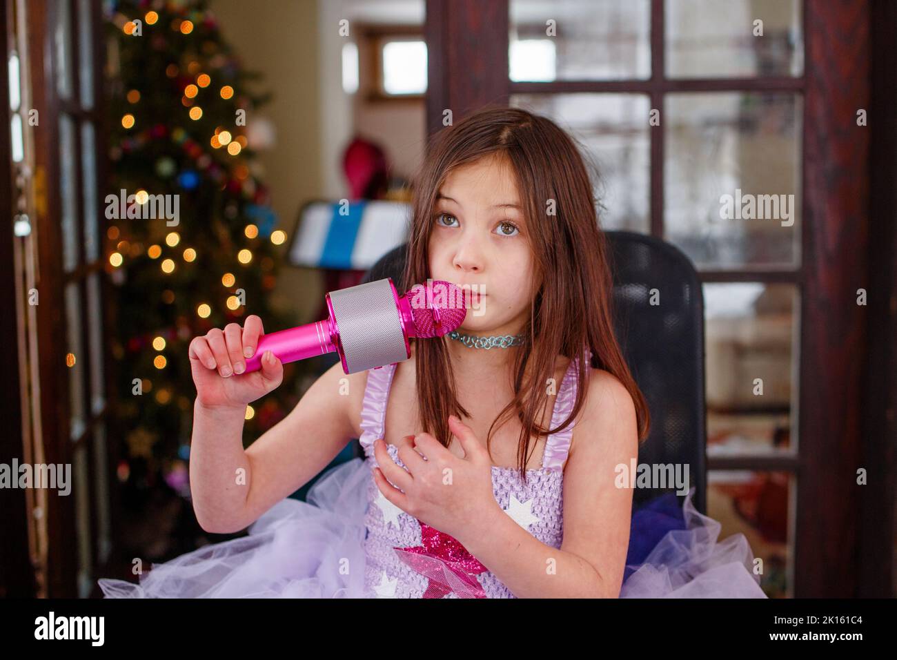 An earnest girl in tutu sings into a pink microphone at home Stock Photo