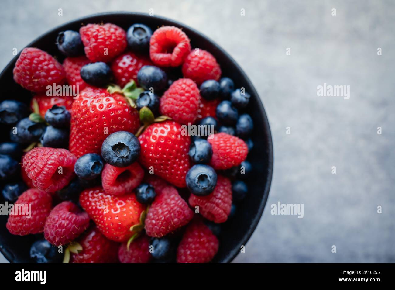 Overhead of bowl of fresh mixed berries on grey background. Stock Photo