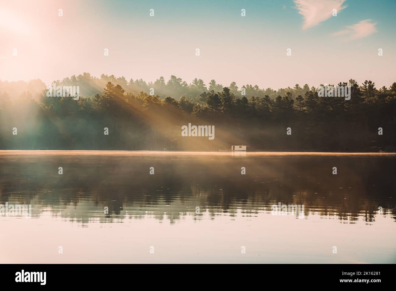 Beautiful light rays shining on a calm lake in the early morning. Stock Photo