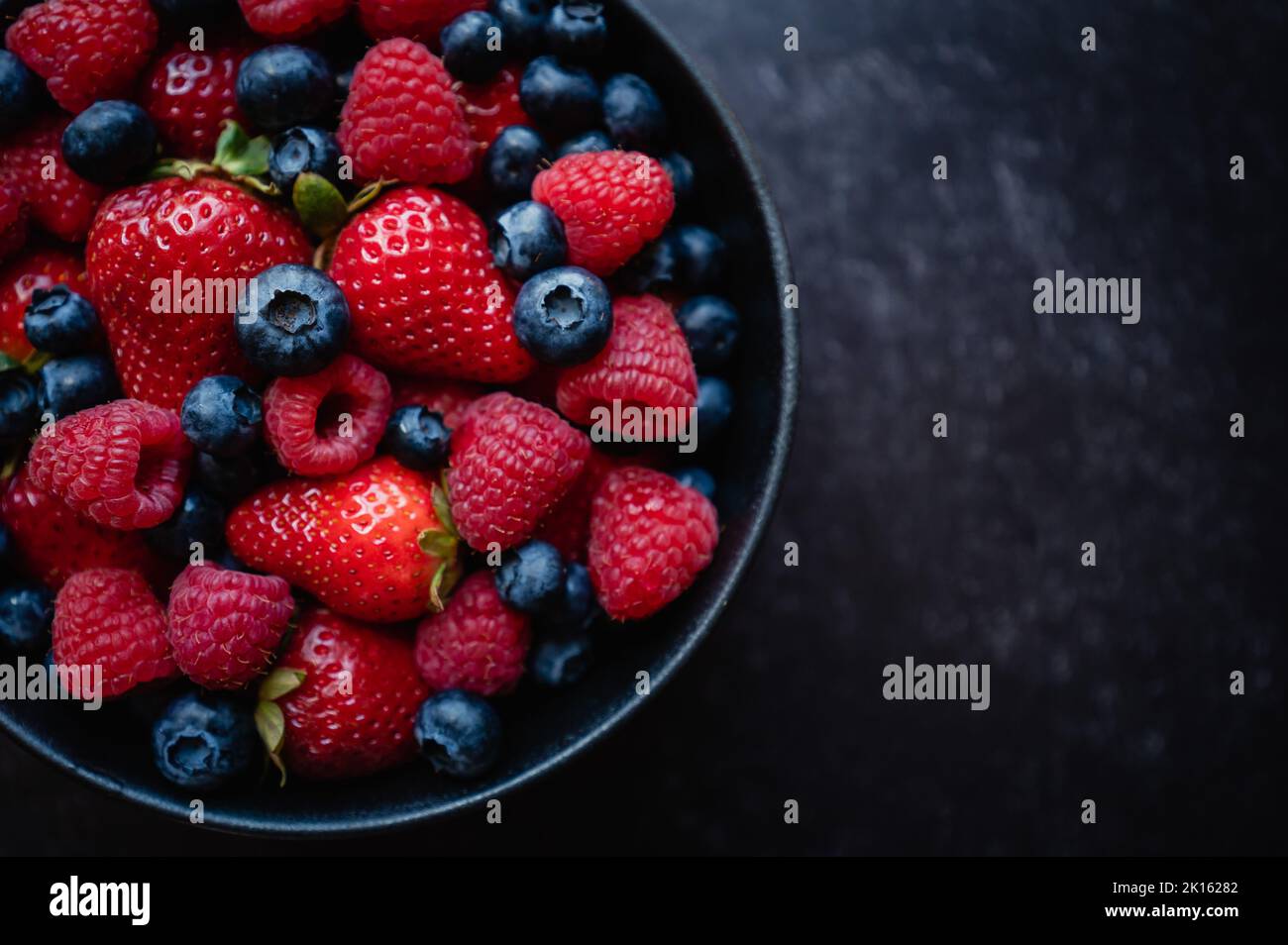 Overhead of bowl of fresh mixed berries on black background. Stock Photo