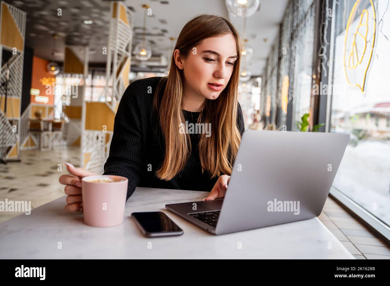 young girl in a cafe by the window working on a laptop Stock Photo - Alamy