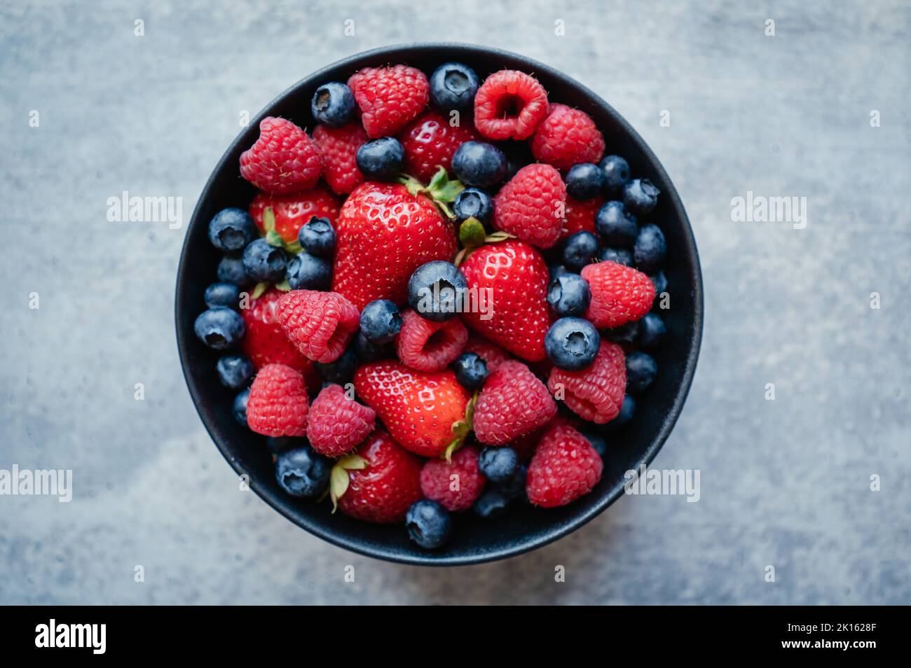 Top view of bowl of fresh mixed berries on grey background. Stock Photo