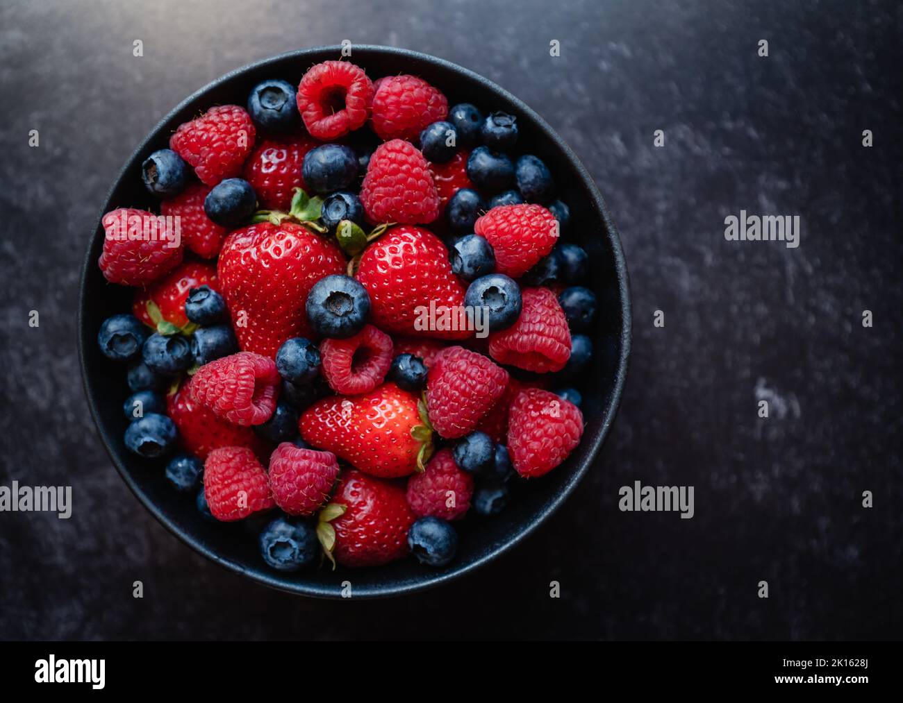 Top view of bowl of fresh mixed berries on black background. Stock Photo