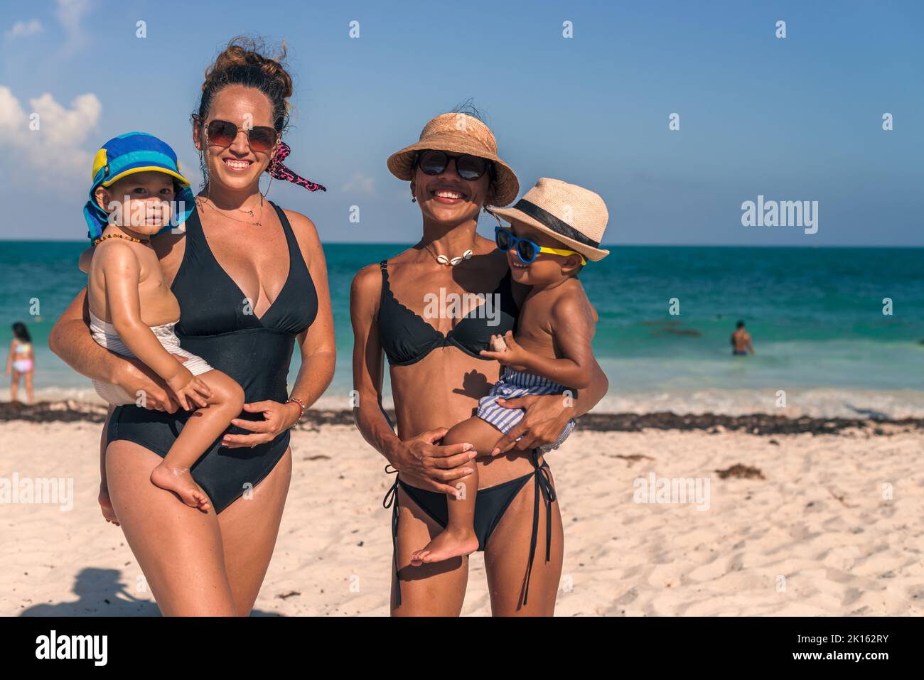 Two Latin Moms Carrying Her Babies At The Beach On A Sunny Day Stock Two latin moms carrying her babies at the beach on a sunny day stock