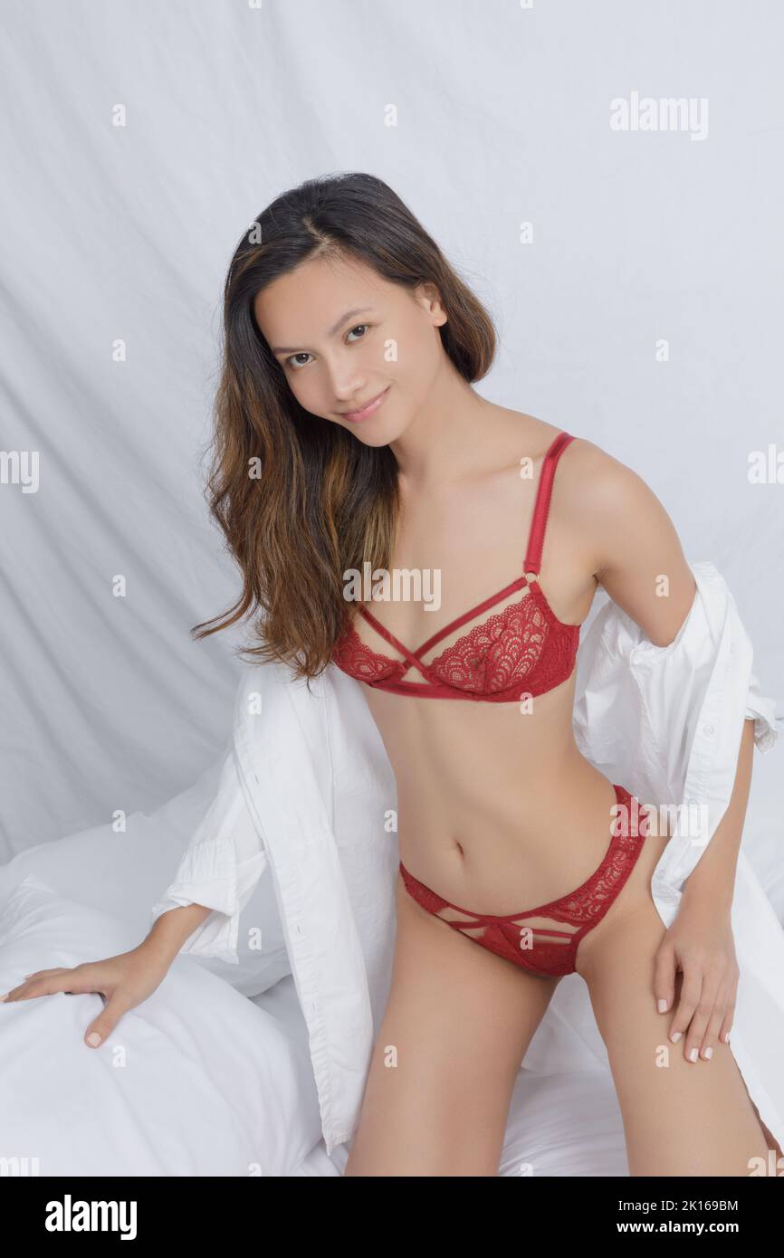 Beautiful Asian woman wearing sexy red  panties and a men's white shirt on a bed with white sheets Stock Photo
