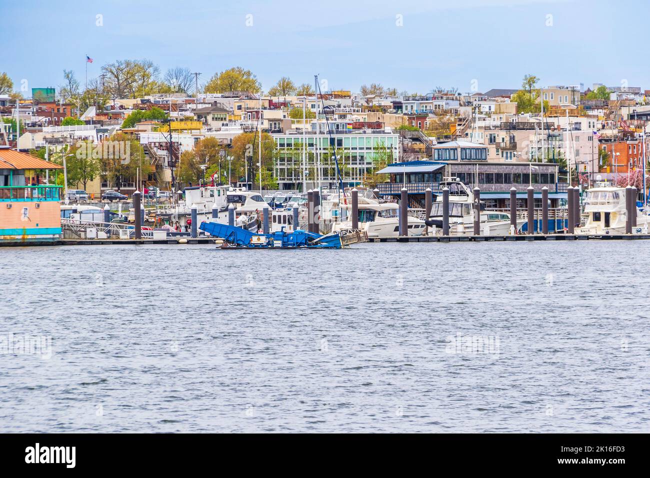 Trash-skimmer boat in Baltimore Inner Harbor, Baltimore, Maryland with background of row houses with view of harbor. Stock Photo
