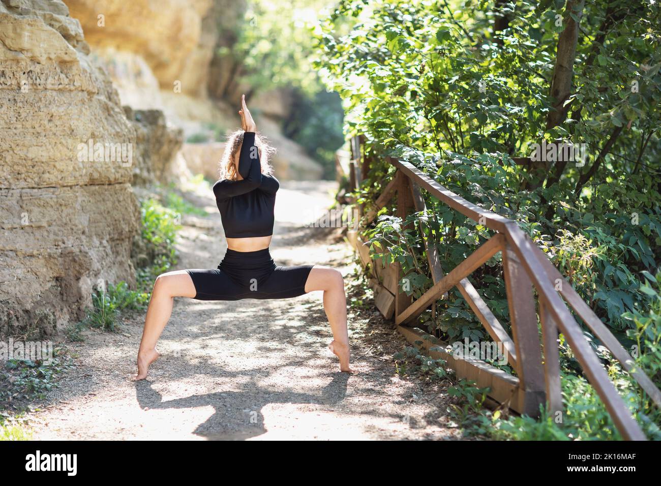 Young woman in black sportswear practicing yoga doing Utkata Konasana exercise, goddess pose, exercising in the park on a warm summer morning Stock Photo