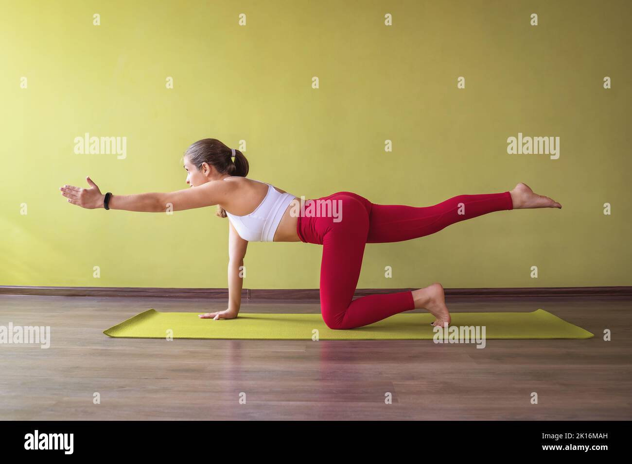 Woman in sportswear practicing yoga doing Parshva Marjariasana exercise, crane pose, exercising in the studio near the wall on the mat. Healthy lifest Stock Photo