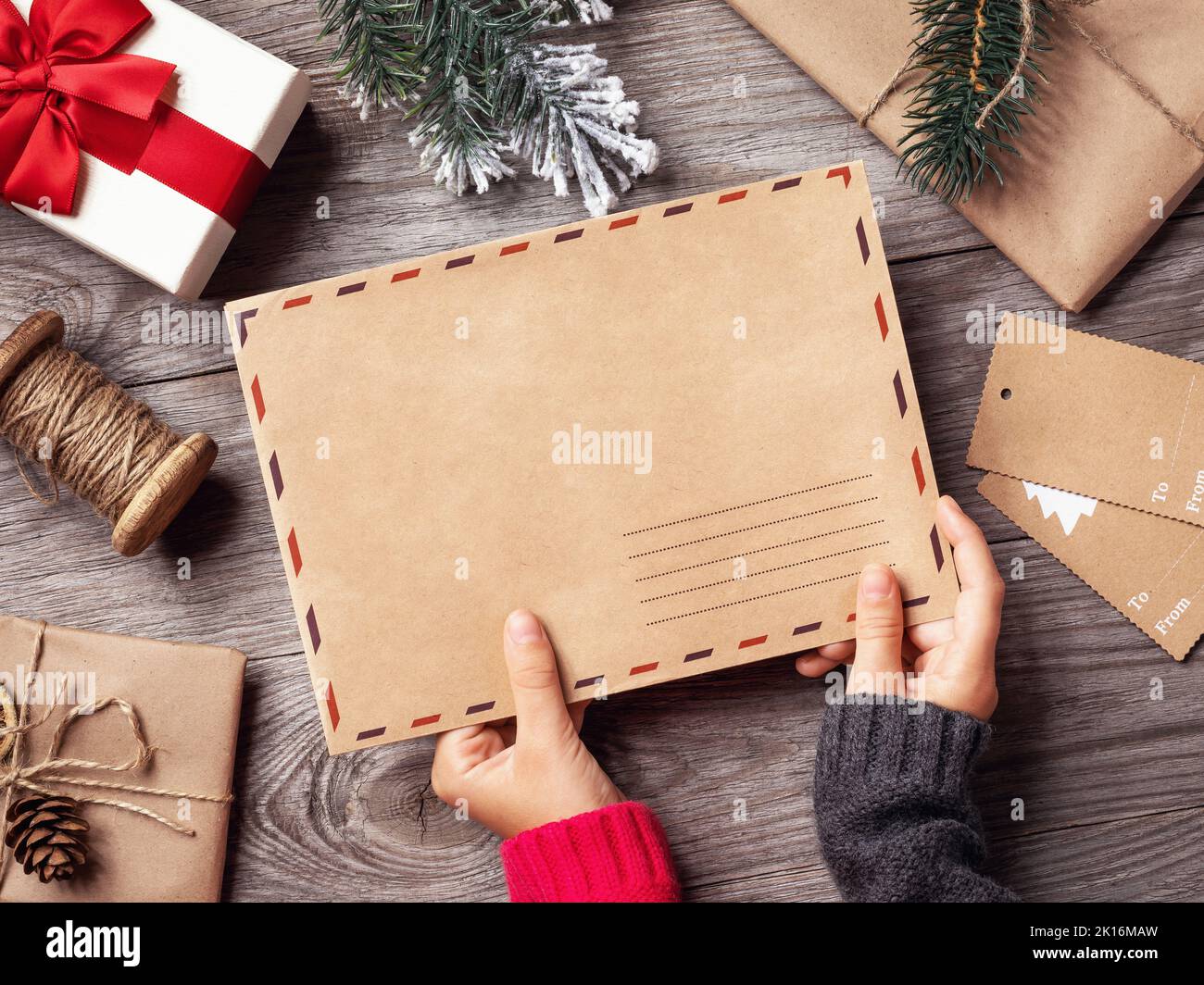 The child holds in his hands an envelope with a letter to Santa Claus on the background of Christmas decorations, a template for the designer Stock Photo