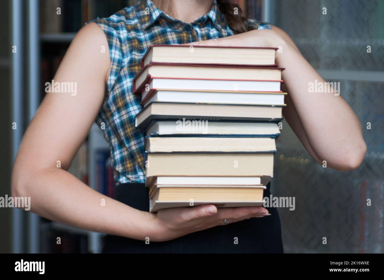 Woman carrying stack of books on the background of a bookcase Stock