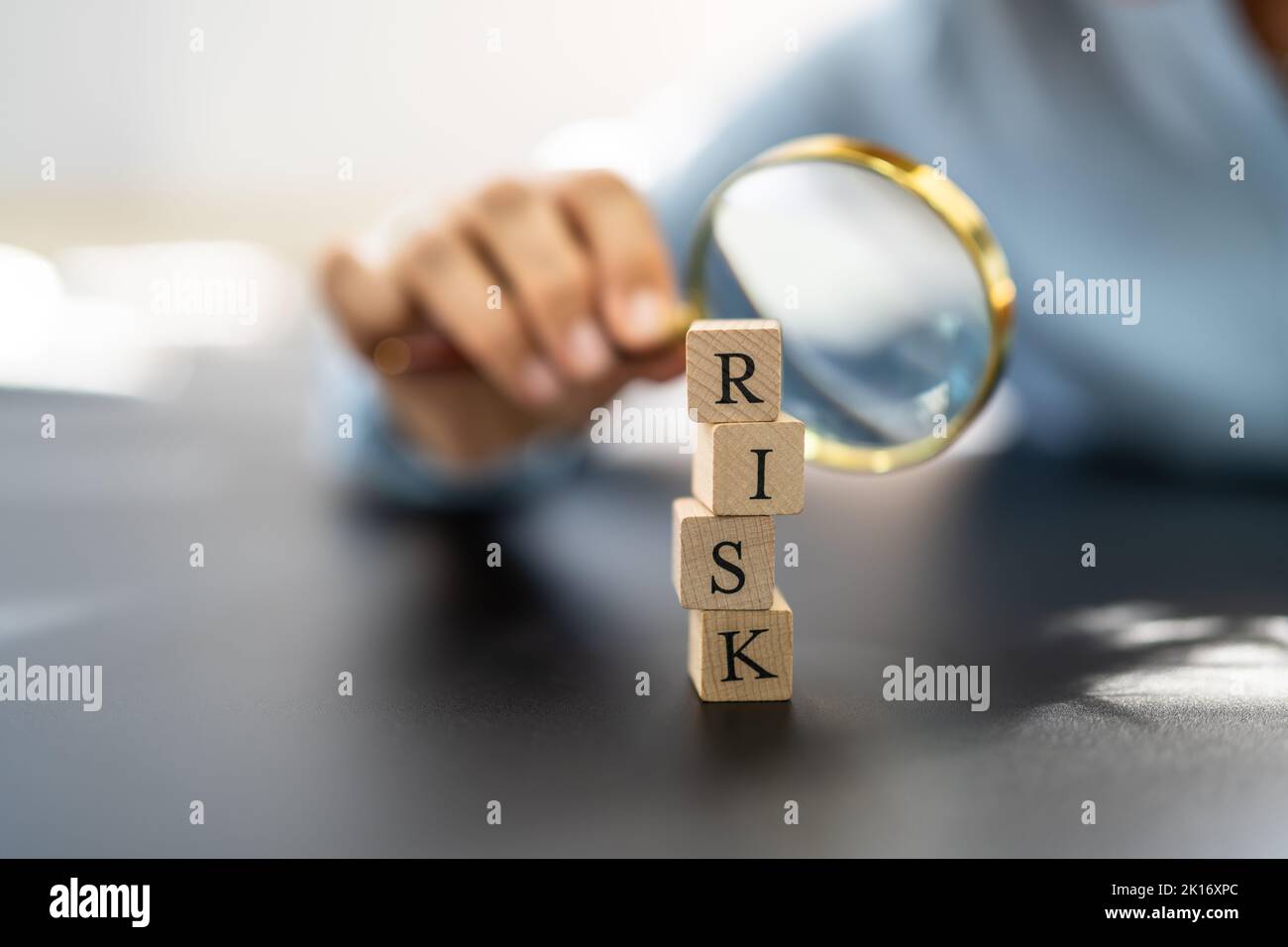 Hand Looking At Risk Blocks Through Magnifying Glass On Wooden Desk Stock Photo