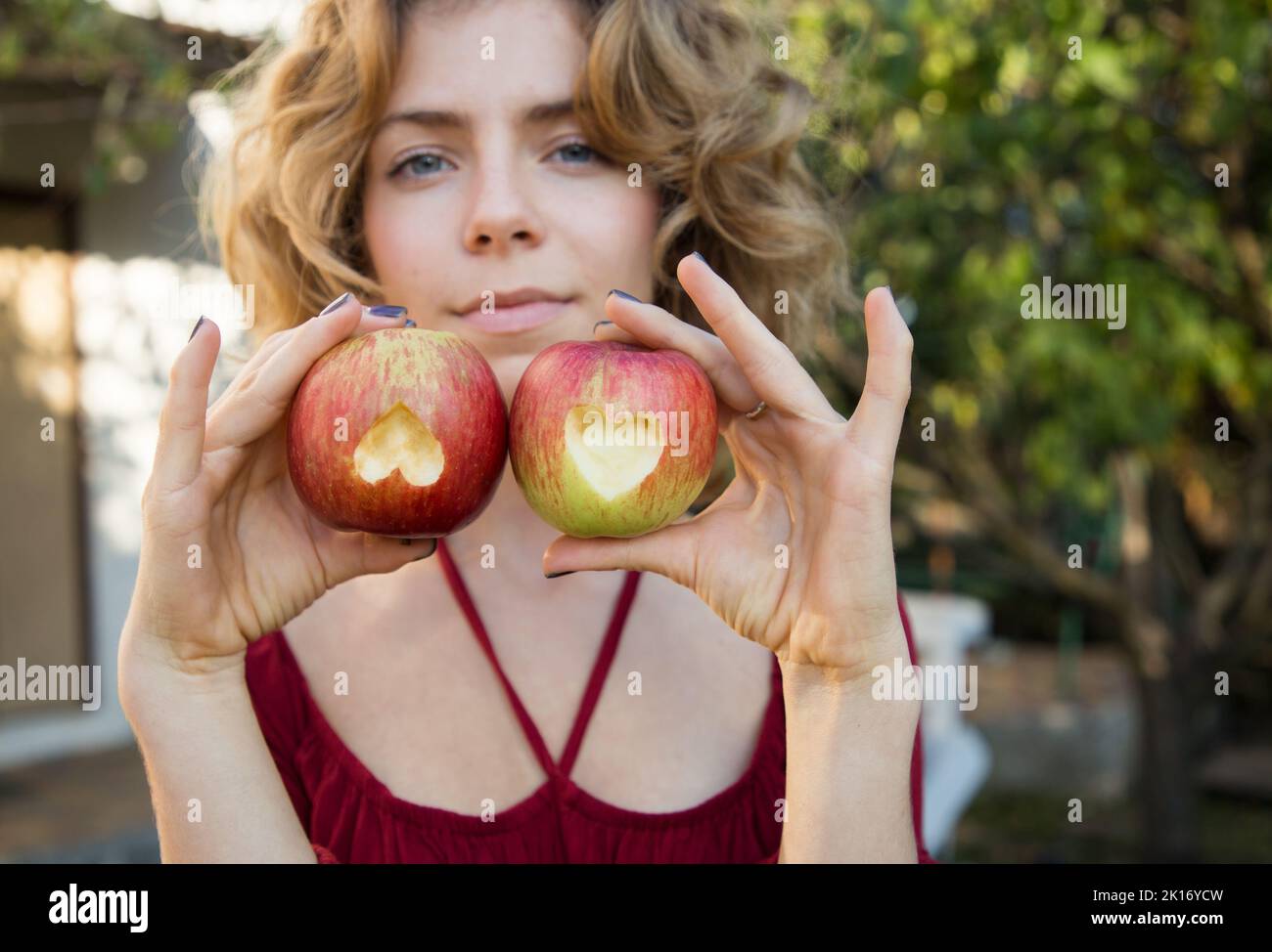beautiful young woman 18 - 20 years old holds in hand two apples with hearts carved into them. focus on apples. Proper vitamin nutrition, diet. Surpri Stock Photo