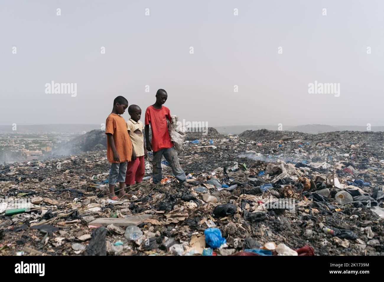 Three African boys exposed to injuries and serious illnesses looking for usabele items in a big urban junkyard; concept of lack of hygiene and health Stock Photo