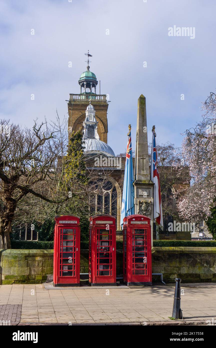 Northampton town centre view with three red telephone boxes in front of a Lutyens designed war memorial, All Saints church in the background. Stock Photo