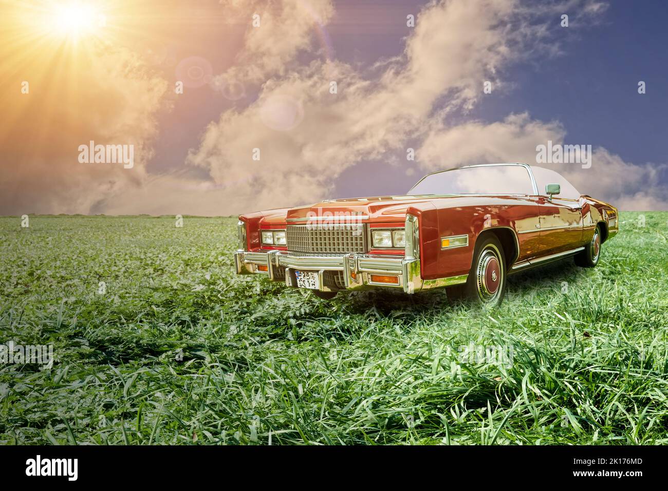 Cadillac convertible, classic road cruiser of American production, on a meadow in front of cloudy sky with sun rays, Vehicle location Lehnin, Germany, Stock Photo