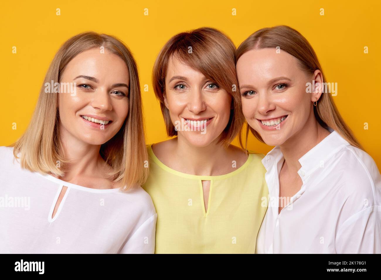 Female happiness. Beauty wellness. Love support. Portrait of three positive women in white yellow blouse together smiling isolated on orange backgroun Stock Photo