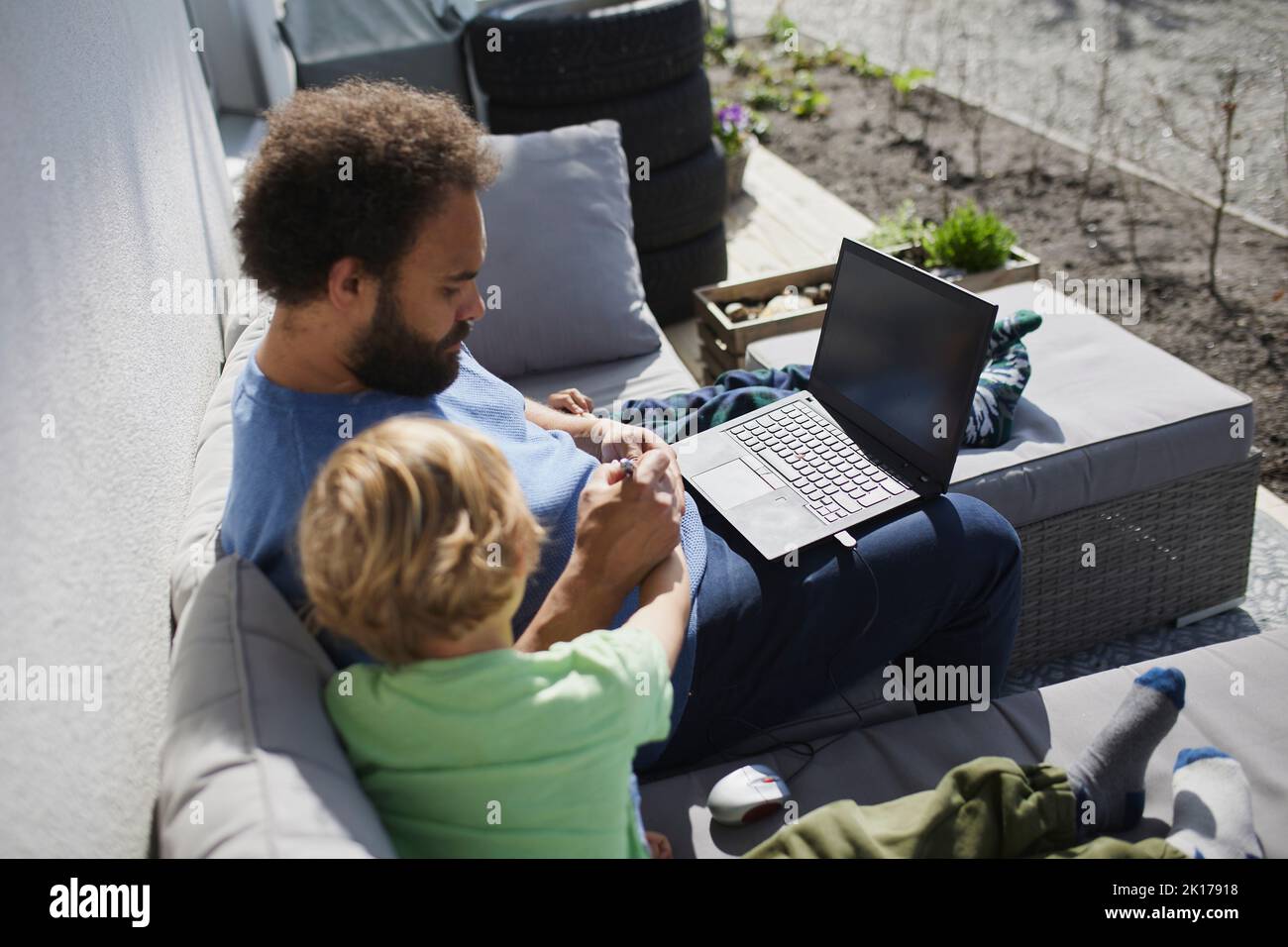 Father sitting with son on deck and working on laptop Stock Photo