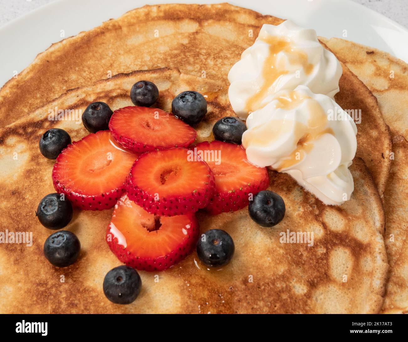 Pancakes with strawberries, blueberries, cream and maple syrup Stock Photo