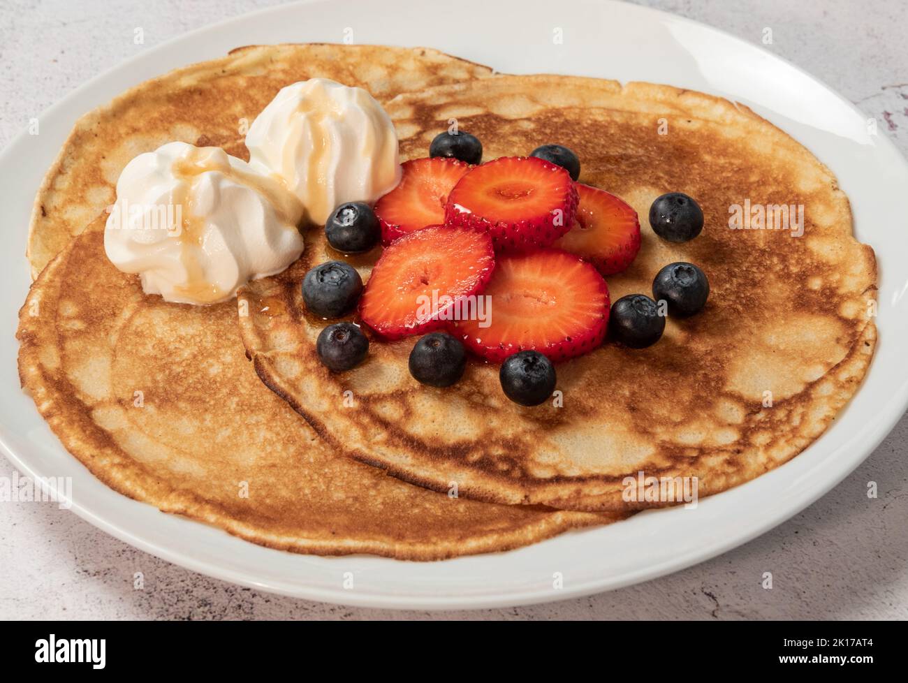 Pancakes with strawberries, blueberries, cream and maple syrup on plate Stock Photo