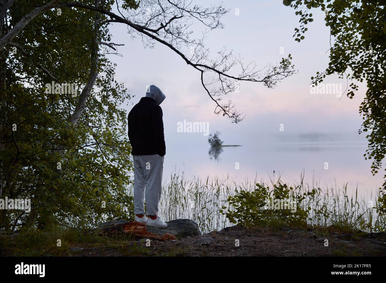 Man standing on lake shore at dusk Stock Photo
