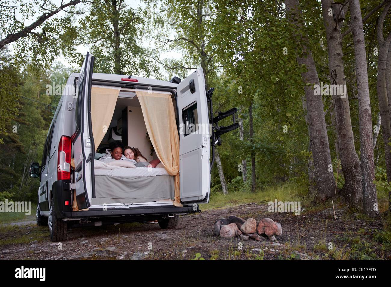 Women lying in bed in camper van parked in forest Stock Photo