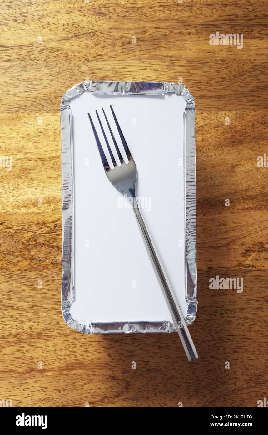 Silver foil takeaway tray with a fork placed on top. Shot from above on wooden table Stock Photo