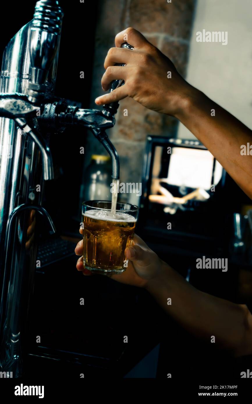 Hand serving beer in glass using tap. Bartender pouring beer while