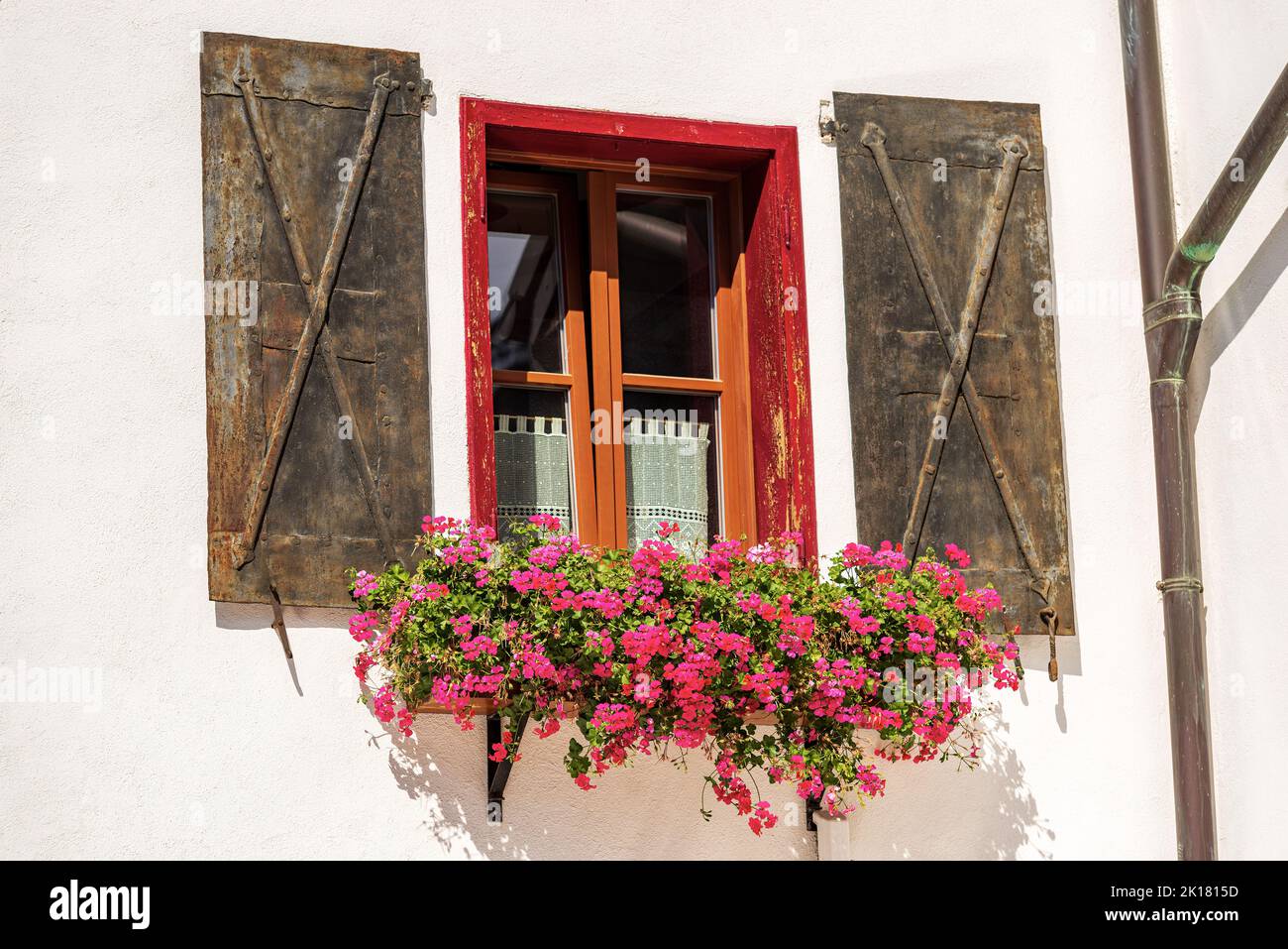 Ancient window with metal shutters and red geranium flowers. Small village of Malborghetto-Valbruna in Val Canale, Udine, Friuli-Venezia Giulia, Italy Stock Photo