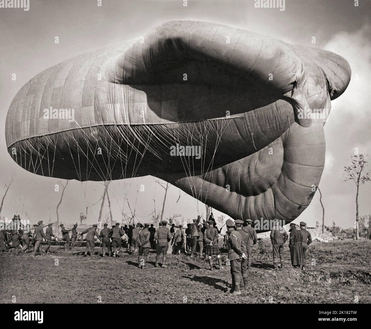 A returning British observation balloon. A small army of men, dwarfed by the balloon, are controlling its descent with a multitude of ropes. They were employed as an aerial platform for intelligence gathering and artillery spotting. The balloons were filled with hydrogen gas, whose flammable nature led to the destruction of hundreds of balloons on both sides. Typically, balloons were tethered to a steel cable attached to a winch that reeled the gasbag to its desired height (usually 1,000-1,500 metres) and retrieved it at the end of an observation session. Stock Photo