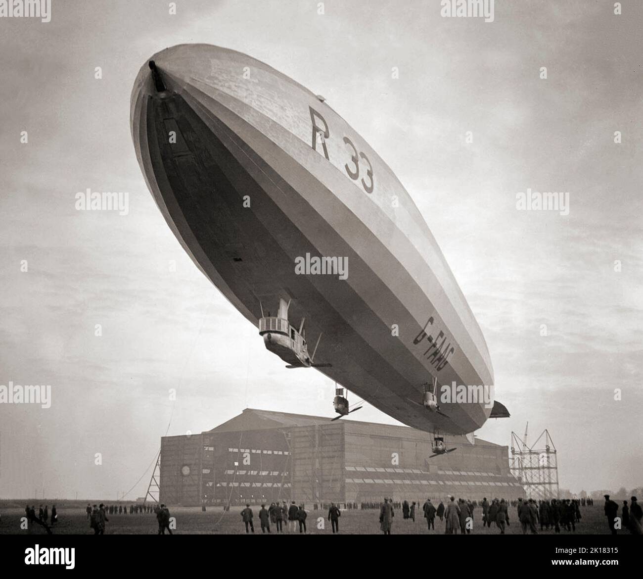 Airship R33 a British rigid airship, flying over its hanger at  RAF Pulham in Norfolk, England in 1925. The airships were built by Armstrong Whitworth for the Royal Naval Air Service during the First World War, but were not completed until after the end of hostilities, by which time the RNAS had become part of the Royal Air Force. Her first flight was in early 1919 then sent to Pulham airship station she clocked up over 300 flying hours in tests and the training of crew. Stock Photo