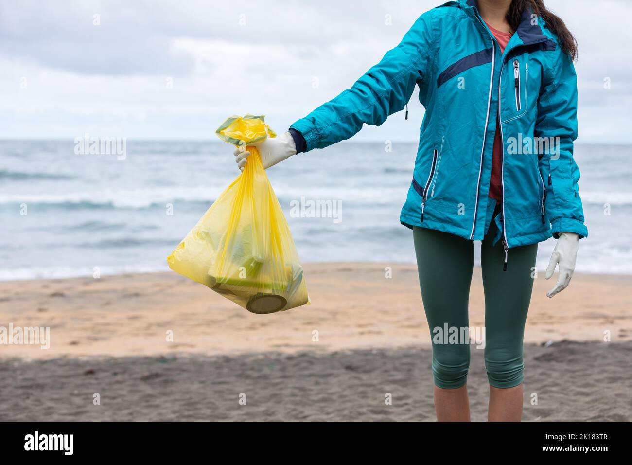 Crop unrecognizable female activist showing bag with collected garbage on seashore Stock Photo