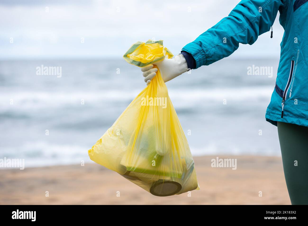 Crop unrecognizable female activist showing bag with collected garbage on seashore Stock Photo