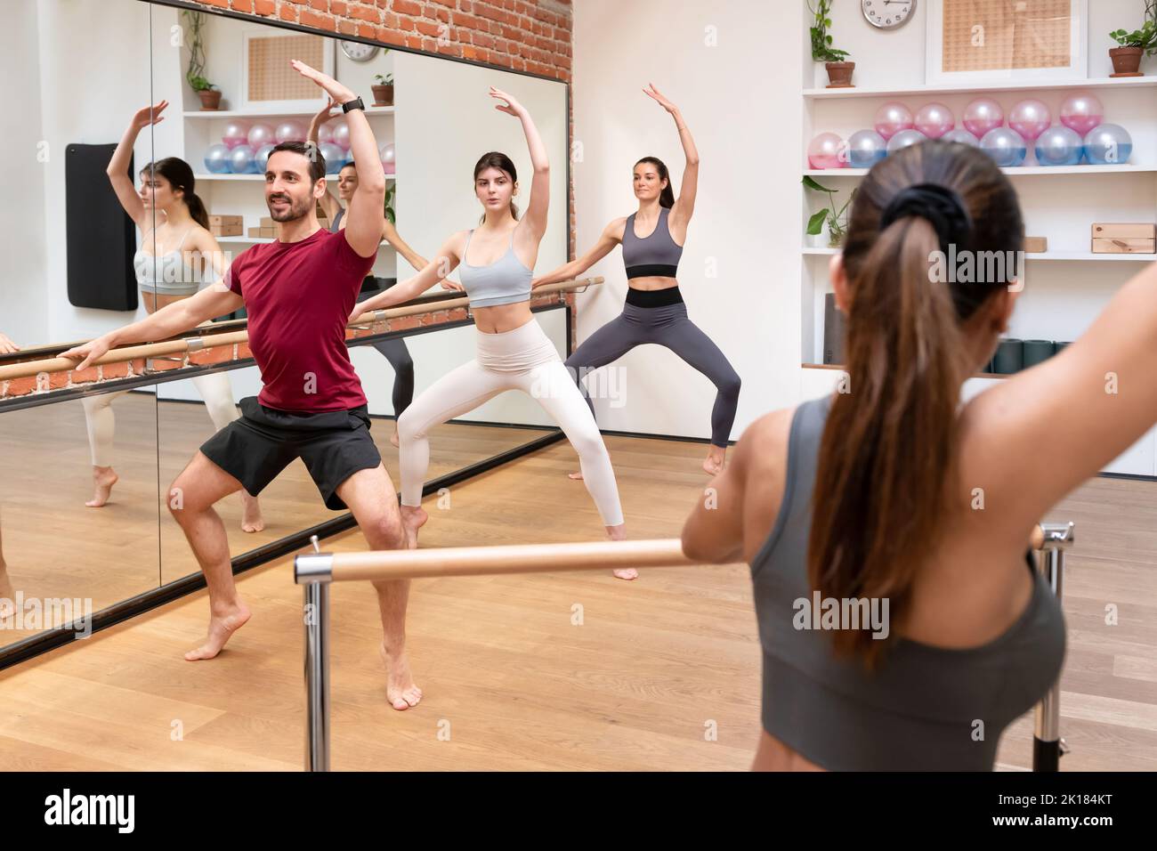 Group of fit people in activewear performing plie squat releve on barre together during class in light studio with mirror Stock Photo