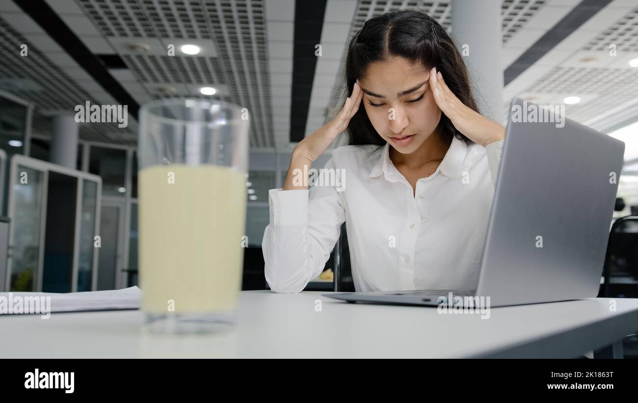 Young tired woman manager sits in office feels headache suffers from pain overwork unhealthy girl office worker feeling unwell migraine pressure Stock Photo
