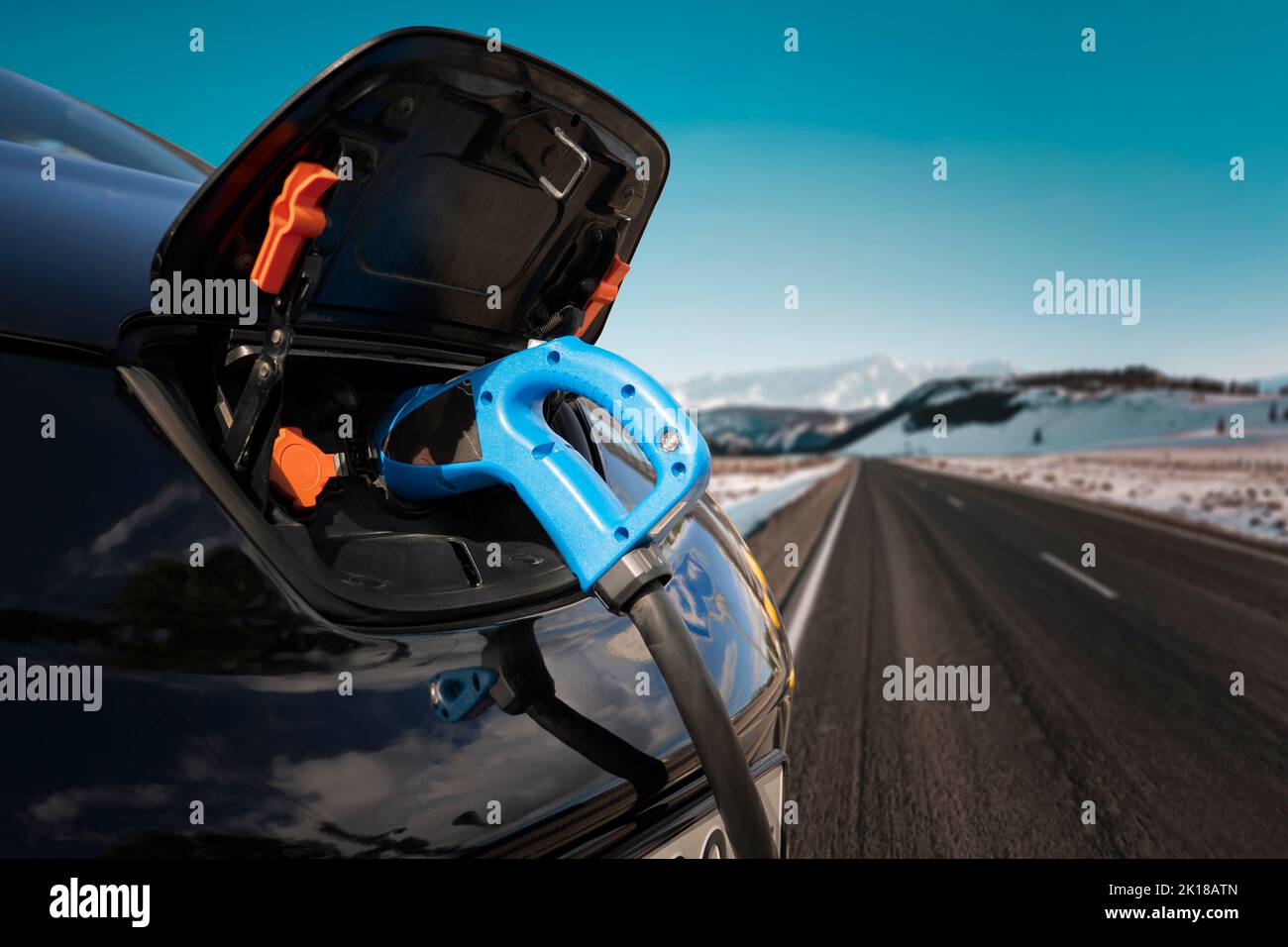 Charging an electric car with the power cable supply plugged in on the road in winter against the background of nature and mountains Stock Photo