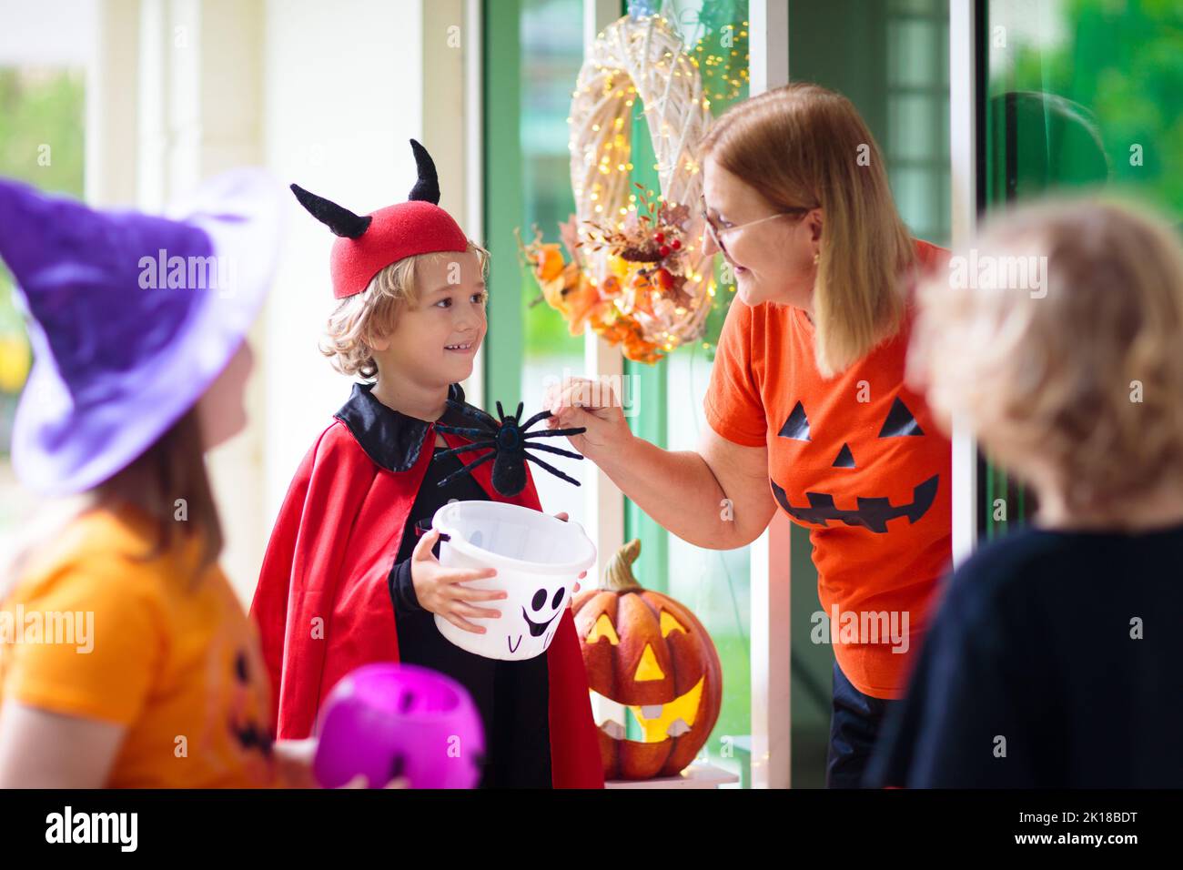 Kids trick or treat on Halloween night. Child at decorated house door. Boy and girl in witch and vampire costume and hat with candy bucket and pumpkin Stock Photo