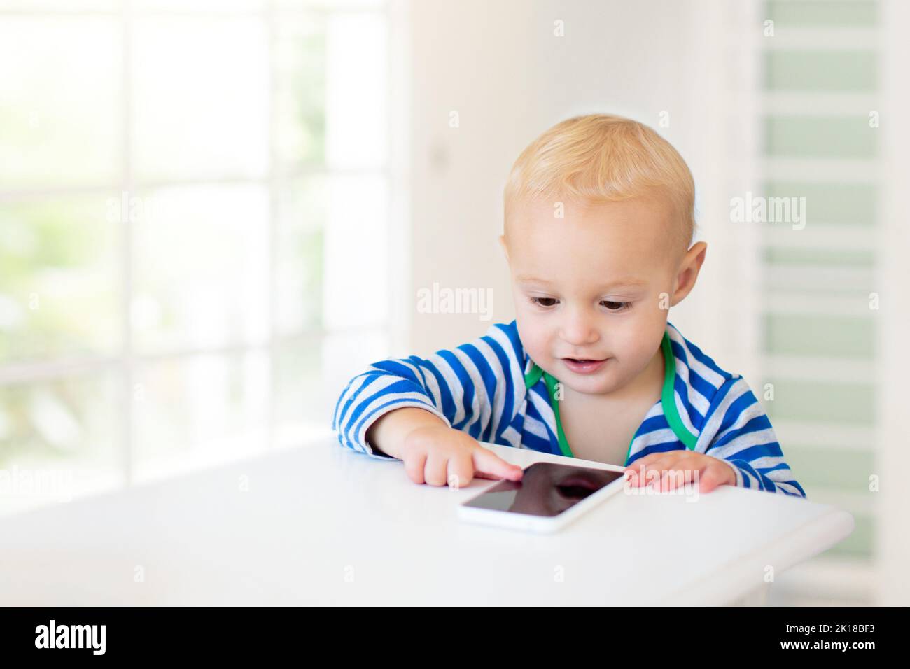Baby boy with mobile phone. Little child trying to play with cell phone. First educational game apps for toddler. Infant and technology. Kid playing w Stock Photo