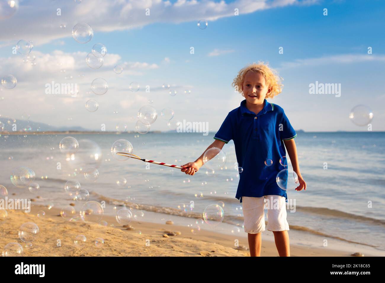 Kids blow bubbles at tropical beach. Child blowing soap bubble playing at sea. Family summer vacation with young kid. Outdoor beach activity for child Stock Photo