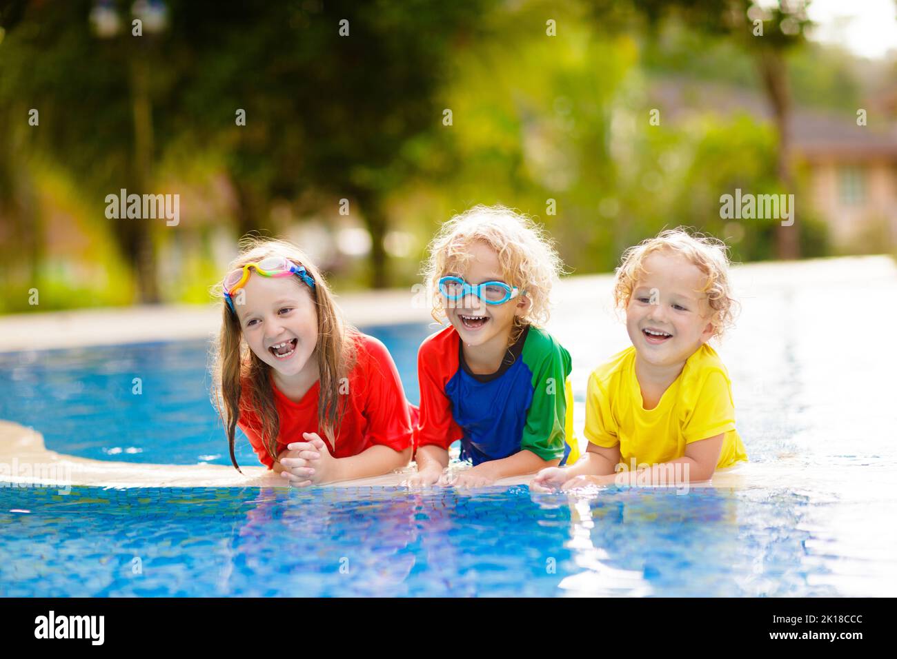 Kids play in swimming pool. Children learn to swim in outdoor pool of tropical resort during family summer vacation. Water and splash fun for young ki Stock Photo