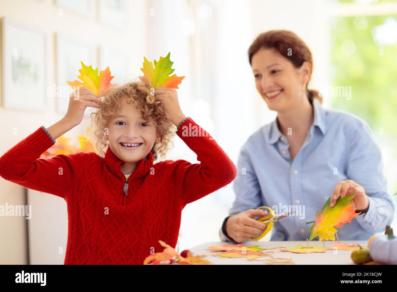 Autumn home decoration. Family decorating house with colorful maple leaves banner. Thanksgiving or Halloween celebration in white living room. Child w Stock Photo