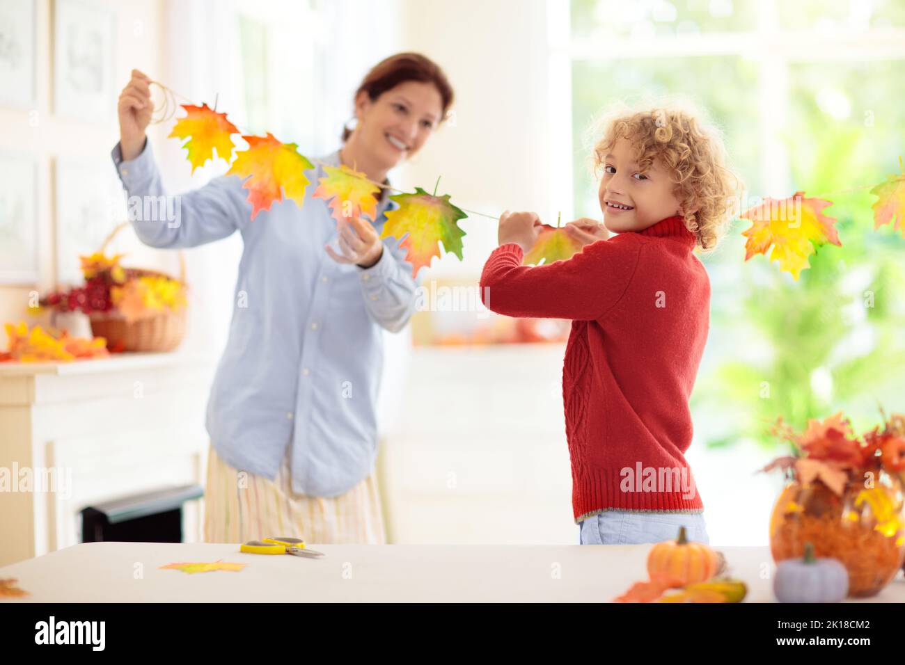 Autumn home decoration. Family decorating house with colorful maple leaves banner. Thanksgiving or Halloween celebration in white living room. Child w Stock Photo