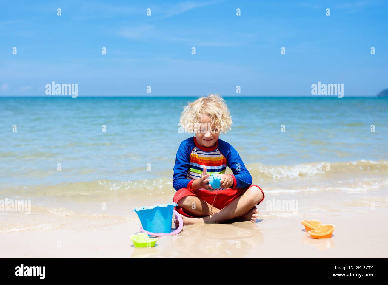Kids playing on tropical beach. Children play at sea on summer family vacation. Sand and water toys, sun protection for young child. Little boy diggin Stock Photo