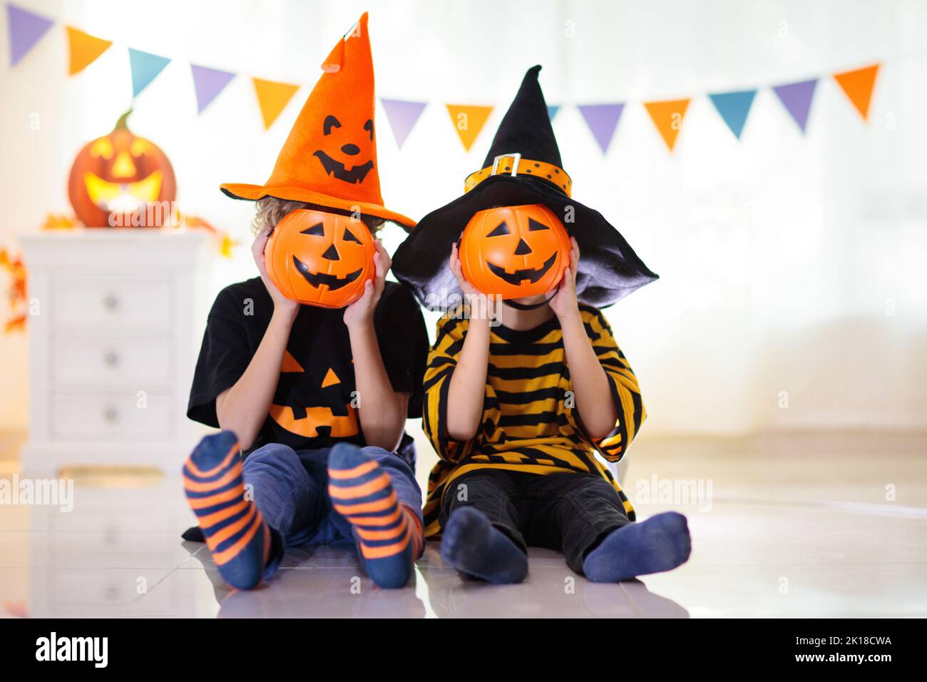 Little girl and boy in witch costume on Halloween trick or treat. Kids holding candy in pumpkin lantern bucket. Children celebrate Halloween at decora Stock Photo
