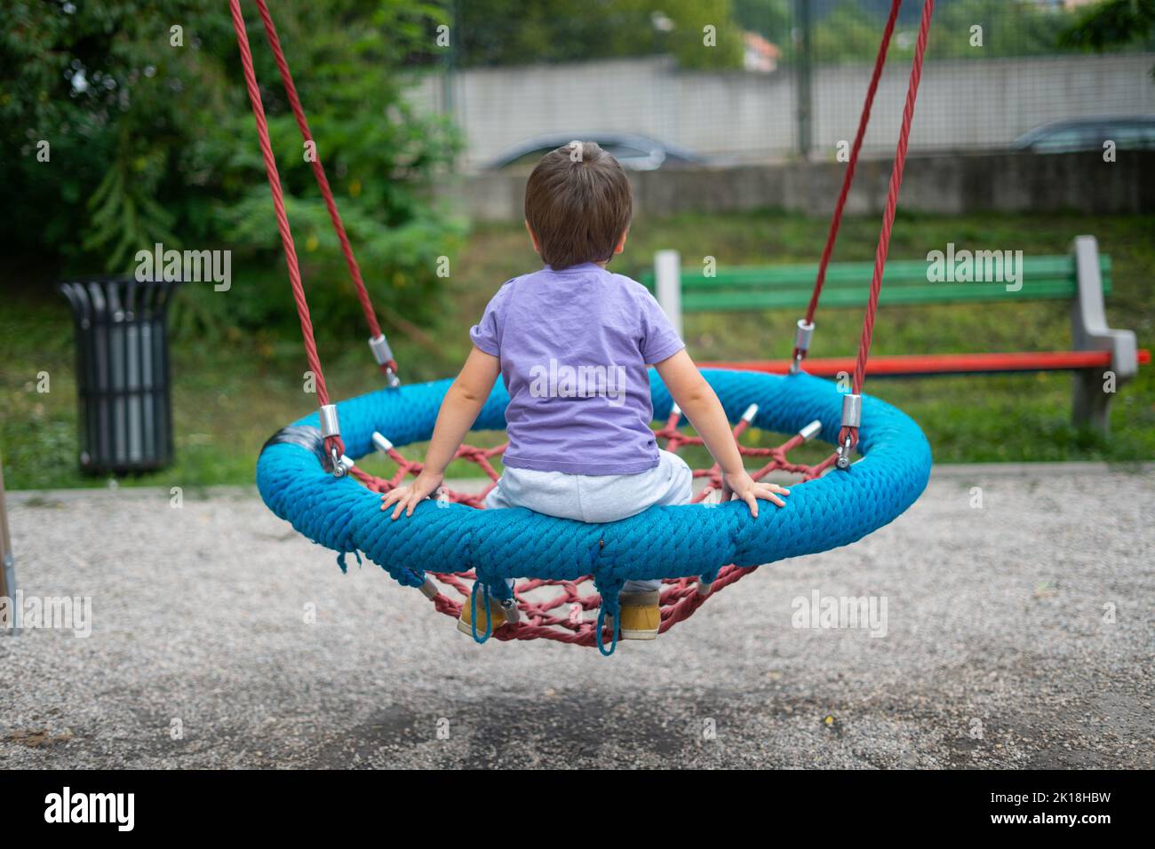 A boy (not recognizable) swings on a rope swing in a children's park