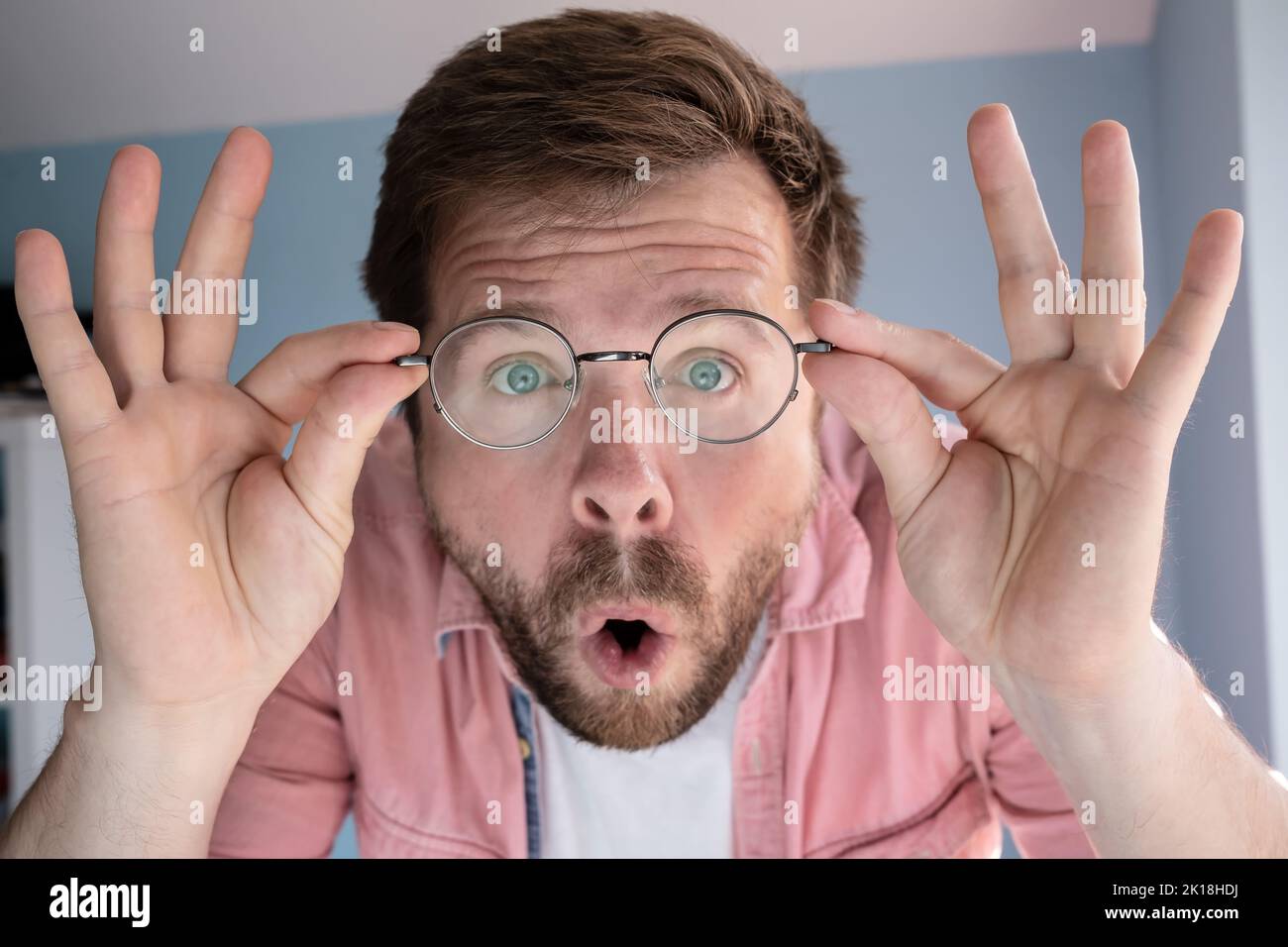 Man is amazed, he does not believe eyes, holds his glasses with hands and opens mouth in surprise. Close-up. Stock Photo
