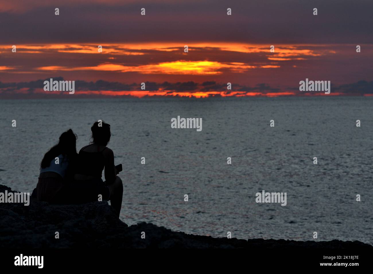 Sunset at Cala Blanca, near Cuitadella, Minorca, featuring couples silhouetted against the sky Stock Photo