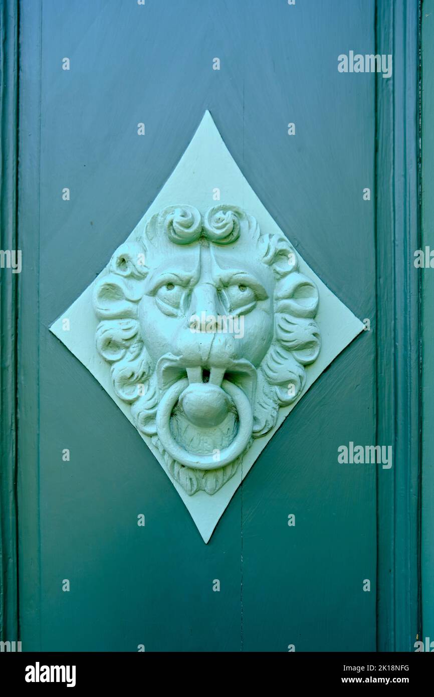 Old vintage door knocker depicting a lion's face on the coffered panel of a green door leaf. Stock Photo