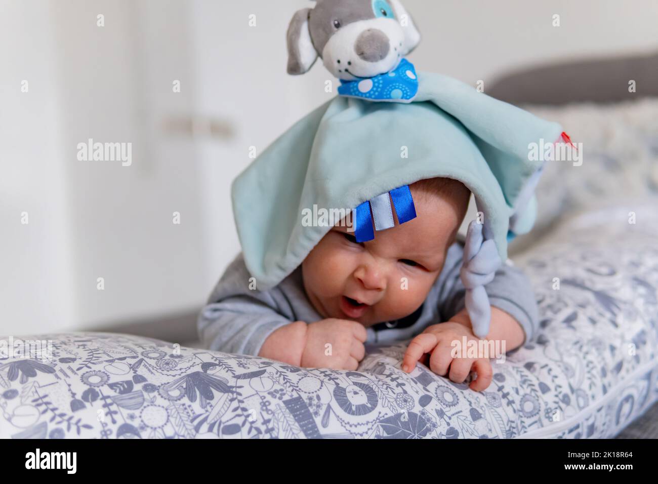 sleepy baby yawns on the pillow with a toy cap on his head Stock Photo