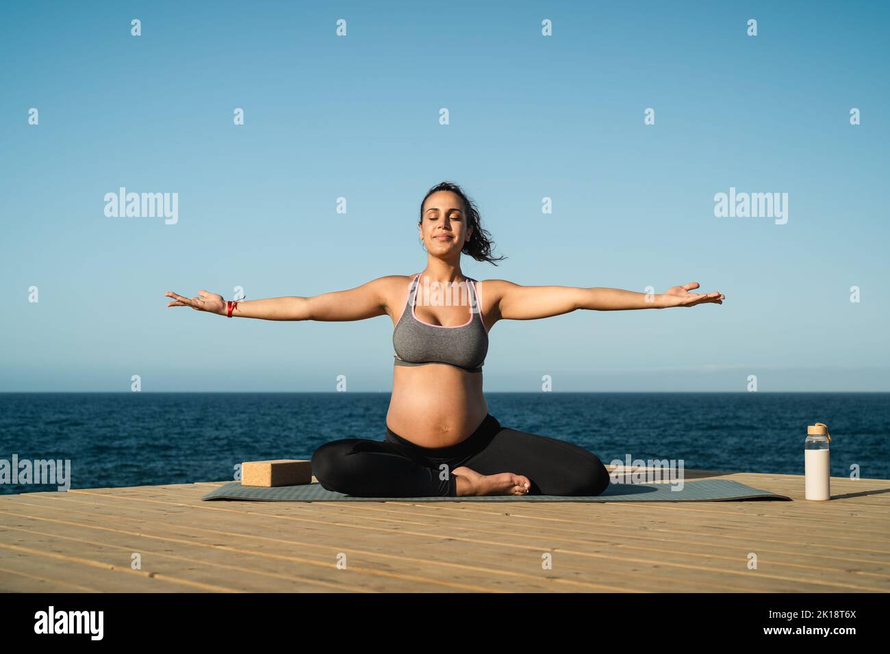 Young pregnant woman doing yoga session next the sea - Meditation and maternity concept Stock Photo