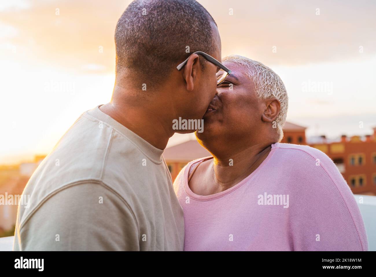 Happy Latin senior couple having romantic moment kissing on rooftop during sunset time - Elderly people love concept Stock Photo